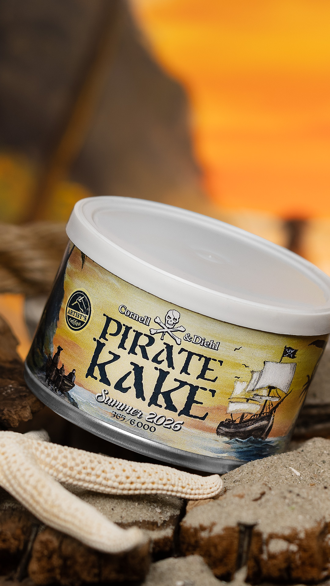 A tin of Cornell & Diehl Pirate Kake Summer 2026 Artist's Edition on sand beside a starfish