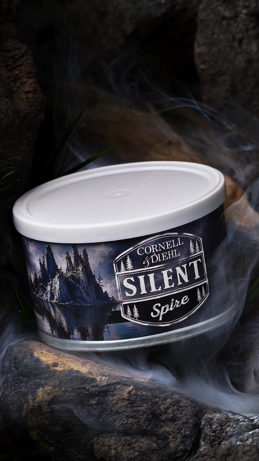 A tin of Cornell & Diehl Silent Spire pipe tobacco on dark rocks wreathed in smoke