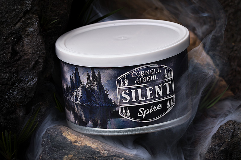 A tin of Cornell & Diehl Silent Spire pipe tobacco nestled among dark rocks and drifting smoke