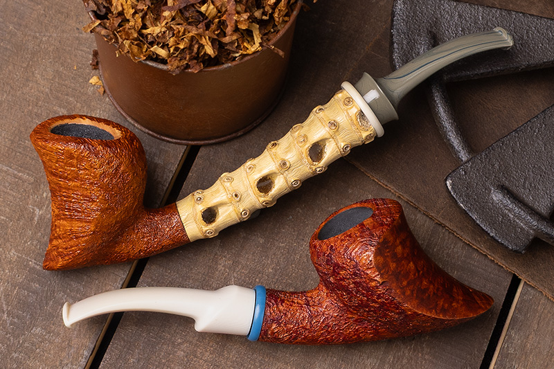 Two Todd Johnson sandblasted freehand pipes, one with a carved bamboo shank, beside a tin of loose tobacco