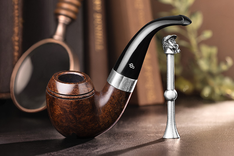 Peterson bent briar pipe with silver band beside a pewter pipe-smoker tamper